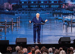 A man in a suit stands on a stage in front of a large crowd. AI generated content