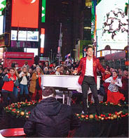 A man in a red jacket is singing on a stage in a crowded city square. AI generated content